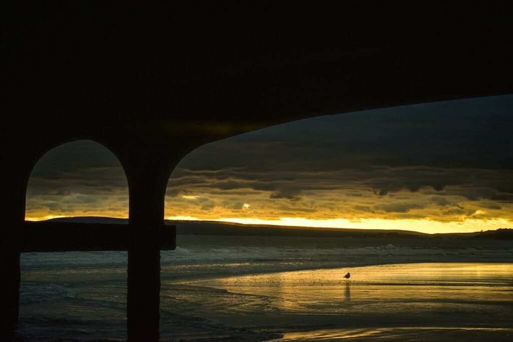 Silhouette of a person walking on a beach at sunset.
