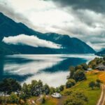 green trees near lake and mountains under white clouds during daytime